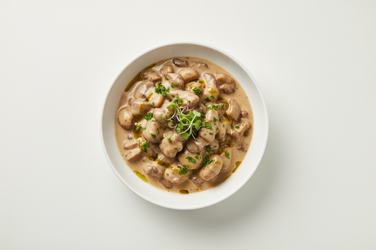 Realistic packshot of porcini mushrooms in creamy sauce, vegetarian, in a white bowl, isolated on plain light background, e-commerce food photography.
